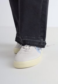 Hvite joggesko med lys blå aksent, teksturert gummisåle og snøring, kombinert med sorte denim-bukser med rå ender.