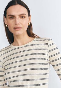 Beżowa bluzka w prążki z poziomymi granatowymi paskami. Ma okrągły dekolt i długie rękawy, co zapewnia dopasowany wygląd.