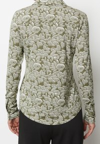 Camicia a maniche lunghe in verde oliva con un motivo astratto bianco. Presenta un colletto e un orlo arrotondato, realizzata in un tessuto testurizzato.