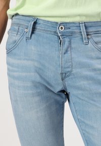 Jeans de denim azul claro con un diseño clásico de cinco bolsillos, cierre de botón y un ligero desgaste para un aspecto casual.