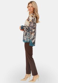 Koszula z nadrukiem w kwiaty w kolorach niebieskim, beżowym i brązowym; zestawiona z brązowymi spodniami i cielistymi szpilkami. Długie rękawy z marszczeniami przy mankietach.
