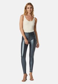 Leggings teal lucidi a vita alta con chiusura frontale a cerniera, abbinati a un top a canotta bianco a coste e tacchi trasparenti.