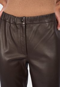Pantalon en simili cuir marron foncé avec une texture lisse, une taille élastique et une fermeture à bouton à l'avant. Présente un ajustement élégant et cintré.