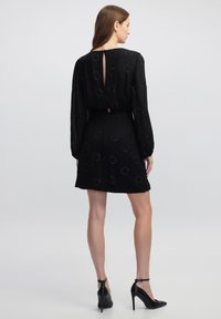 Schwarzes Kleid mit langen Ärmeln, kreisförmigen Mustern und einem Schlüsselloch-Detail im Rücken. Glatte Textur mit taillierter Passform und ausgestellt Rock.