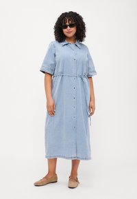 Lyseblå denimkjole med korte ermer, knappelukking foran og belte i midjen. Den har en rett snitt og subtil kantdetalj.