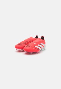 Bright red soccer cleats with a textured upper, featuring ventilation holes and three white stripes on the side, equipped with clear studs.