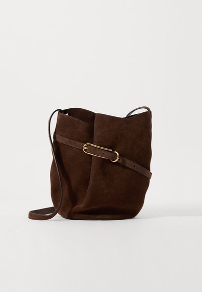 Geantă bucket din suede maro cu un accent din metal auriu, având o curea lungă pentru umăr și o suprafață moale, texturată. Design minimalist.