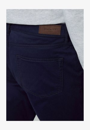 Navy blue chinos made of cotton blend, featuring a back pocket and a stitched label at the waistband with "HACKETT LONDON" embossed.