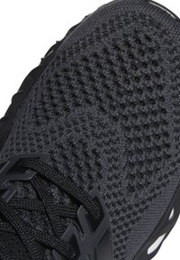 Chaussure de sport noire tricotée avec dessus texturé, lacets noirs passant par des œillets en plastique et bord de semelle coussinée visible.
