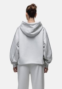 Hoodie corto e oversize in tessuto grigio chiaro, con cappuccio regolabile, spalle basse e dettagli delle cuciture a contrasto lungo le maniche.