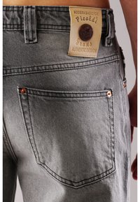 Graue Denim-Jeans mit strukturiertem Finish. Mit einem Lederpatch mit Markenname und Logo, Kupferriegeln und Detailgestaltung der hinteren Tasche.