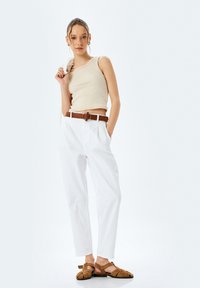 Top in cotone beige a costine, pantaloni bianchi a vita alta con tasche laterali e cintura marrone con fibbia tonda. Sandali pianeggianti marroni completano l'outfit.