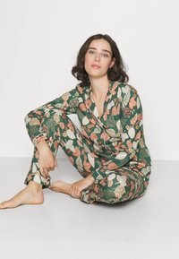 Grünes Pyjama-Set mit Blattmustern in Orange und Creme. Hergestellt aus weichem, leichtem Stoff. Besticht durch ein Knopfverschluss-Oberteil und eine Hose mit elastischem Bund.