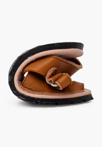 Sandalo in pelle marrone con superficie texturizzata, suola in gomma e cinturino regolabile con dettaglio a cerchio metallico; il design è compatto e piegato.