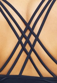 Navy blue swimsuit featuring crisscrossed straps on the back, highlighting smooth, soft texture and a fitted design.