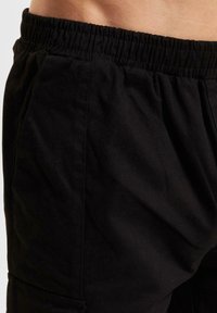 Black shorts with an elastic waistband, made of textured fabric, featuring side pockets and a relaxed fit. Stitches visible on the seams.
