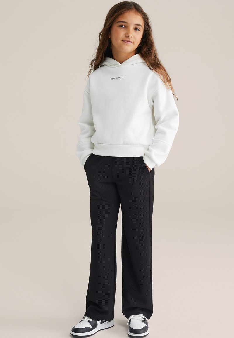 Sweat à capuche blanc avec le texte "SUNDAY BRUNCH" et pantalon large noir tissé. Des baskets noir et blanc complètent l'ensemble.
