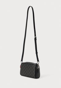 Melnā krustsoma ar tekstūru brūnu rakstu. Ir gluda ādas pamatne un regulējama siksna, kā arī sudraba apdares elementi.