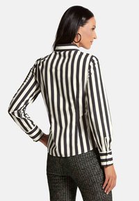 Gestreepte blouse met zwart-witte verticale strepen, lange mouwen, knoopmanchetten en een kraag. Ggedragen met gestikte zwarte broeken.