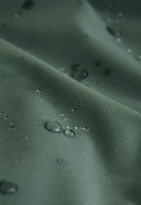 Tela verde resistente al agua con una textura suave, con gotas de agua en la superficie que resaltan su cualidad impermeable.