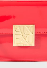 Κόκκινη πατενταρισμένη δερμάτινη τσάντα με χρυσό γεωμετρικό κούμπωμα, με απαλή επιφάνεια και κομψό ορθογώνιο σχήμα.