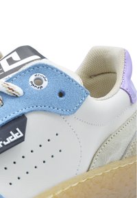 White sneaker featuring light blue suede accents, perforated detailing, black logo, and tan rubber outsole. Smooth and textured materials used.
