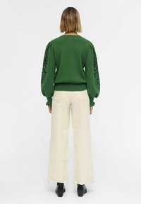 Pull vert à manches bouffantes avec des découpes. Associé à un pantalon crème à jambes larges et des bottines noires.