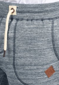 Joggers de punto gris con una apariencia texturizada, que cuentan con un cordón crema y un parche de cuero marrón como acento. Cintura elástica de altura media.