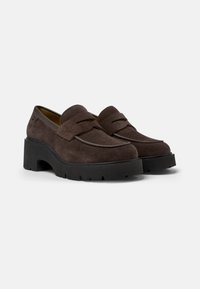 Brown suede loafers with a chunky black rubber sole, featuring a stitched design and dual front straps for secure fit.