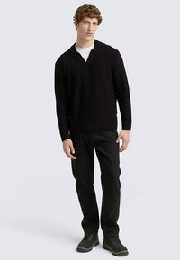 Černý pletený svetr s výstřihem do V, doplněný tmavými kalhotami a trekovými botami. Látka vypadá hladká bez vzorů nebo zdobení.