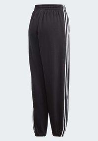 Svarta träningsbyxor med elastisk midja, med tre vita vertikala ränder längs varje sida och tapered design vid bensluten. Mjuk textur.