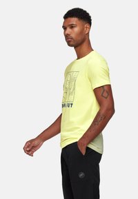 Lys gul bomulds T-shirt med et grafisk design på fronten og rund halsudskæring. Matchende med sorte, lette bukser.