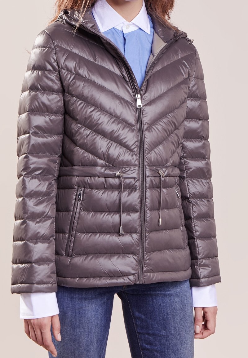 Vadderad, grå jacka med ett chevronmönster, dragkedja fram, dragsko i midjan och sidofickor. Materialet har en blank yta.