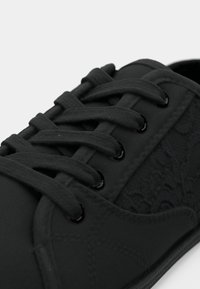 Baskets noires à lacets avec des panneaux en tissu texturé et des œillets métalliques noirs, présentant des coutures détaillées et un motif de lacets latéral.