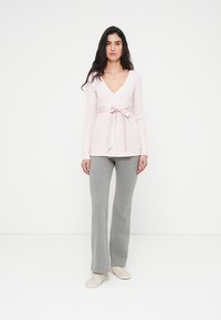 Top de manga larga de color rosa claro con escote en v y lazo en la cintura, combinado con pantalones acampanados grises. La tela parece suave y con textura.