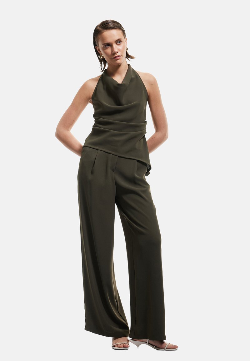 Haut halter vert olive foncé avec un design drapé, associé à un pantalon large. Tissu lisse avec une coupe décontractée et un minimum de détails.