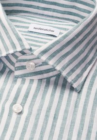 Chemise à col avec des rayures verticales vertes et blanches, boutons en nacre et étiquette de marque "seidensticker" visible à l'intérieur du col.