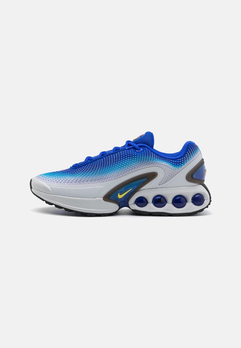 Baskets athlétiques bleues et blanches avec un design en dégradé, semelle extérieure noire, logo Nike jaune, coussins d'air visibles dans la semelle et lacets bleus.