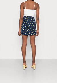 Mörkblå kjol med gult fruktmönster, rynkad midja och en figurnära design. Vit linne och ljusgula klackskor fulländar looken.