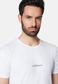 Biała koszulka z okrągłym dekoltem i krótkimi rękawami, z czarnym logo "LANČERTO" z przodu, wykonana z gładkiego, lekkiego materiału.
