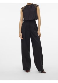 Blouse noire avec manches courtes en dentelle et détail œillet, associée à un pantalon noir taille haute à jambes larges. Tissu lisse, coupe ajustée.