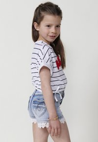 Camiseta blanca a rayas con corazón bordado rojo, combinada con pantalones cortos de mezclilla con encaje en los bordes y bolsillos traseros en forma de corazón.