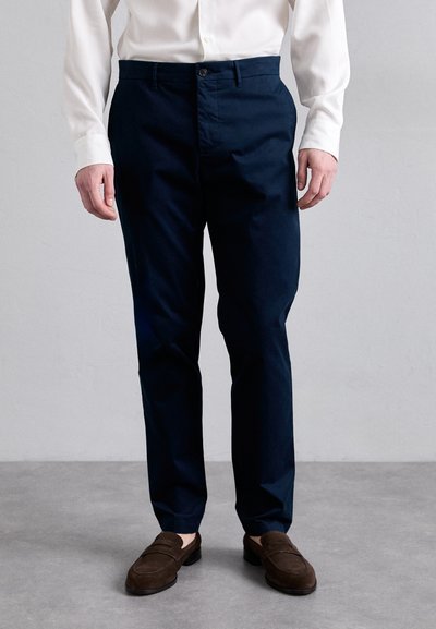 Marineblå chinos lavet af bomuld, med lige pasform, knaplukning og lommer. Båret med brune ruskinds loafers.