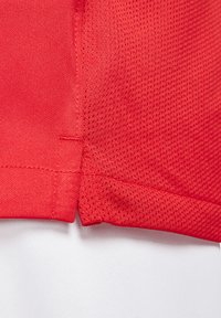 Rotes Sporttrikot mit Mesh-Struktur, ausgestattet mit gestickten Details und einem nahtlosen Übergang zu einem weißen Stoffabschnitt am Saum.