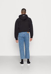 Čierna mikina s kapucňou s crop strihom, skombinovaná so svetlomodrými rovnými džínsami a čiernymi kockovanými slip-on topánkami.