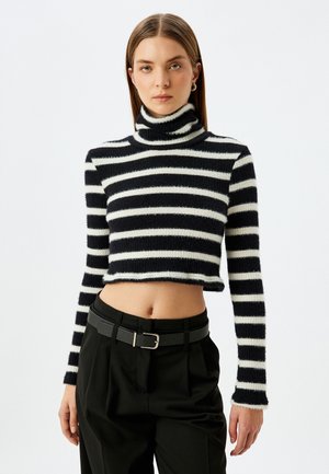 Maglione corto a collo alto a righe bianche e nere con maniche lunghe, realizzato in un morbido tessuto peloso, abbinato a pantaloni neri a vita alta.