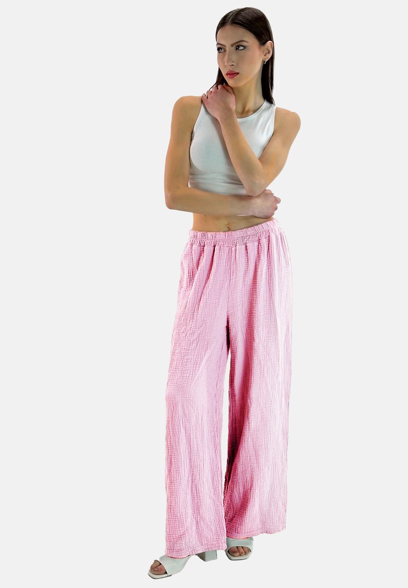 Roze, gekreukelde, wijd-uitlopende broeken met een elastische tailleband en zachte textuur, gecombineerd met een aansluitend wit mouwloos topje en lichte schoenen.