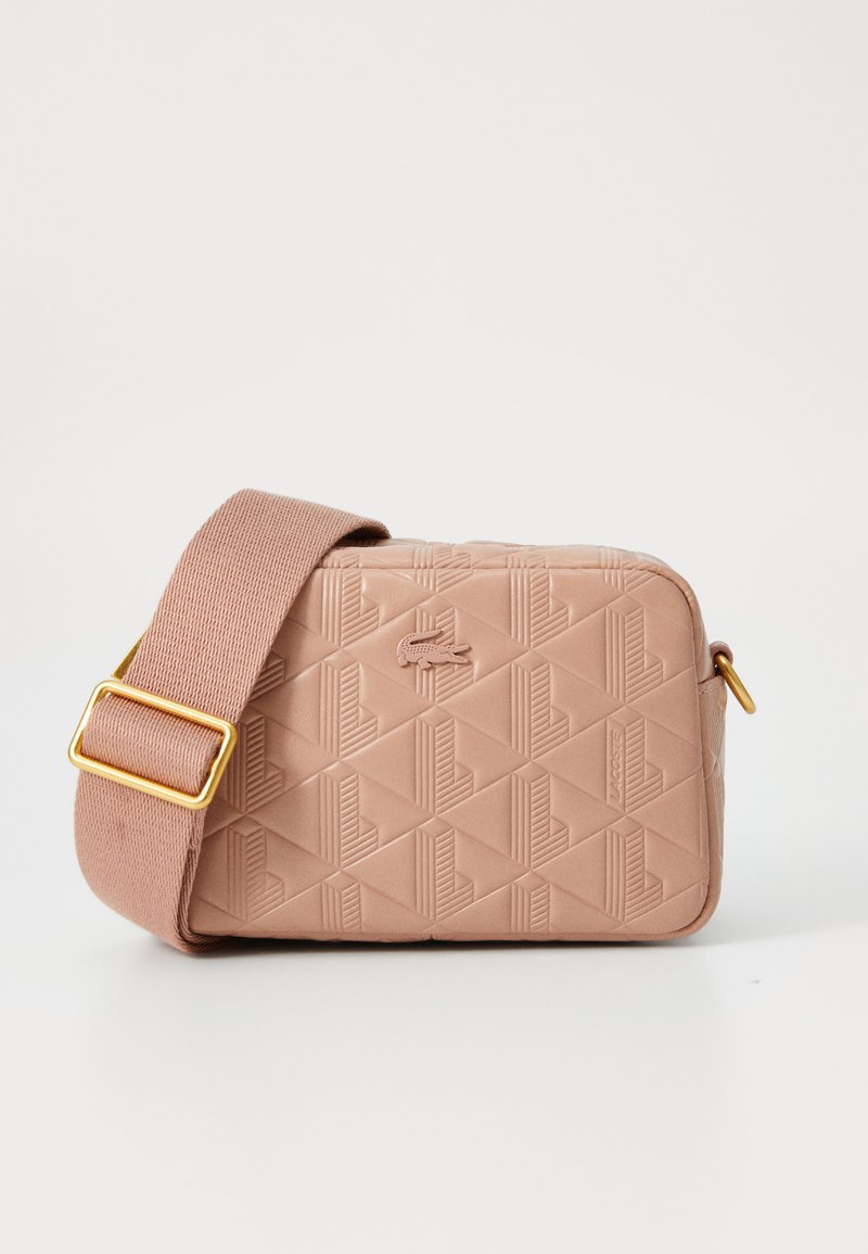 Borsa rettangolare color tan con motivo geometrico in rilievo, texture morbida e una larga tracolla regolabile. Presenta finiture in oro e dettagli con logo.