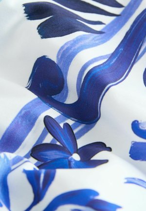 Virágmintás textil, amelyen élénk kék ecsetvonások láthatók egy fehér háttéren, sötétkék virágformák és hullámvonalak alkotják a vibráló mintázatot.