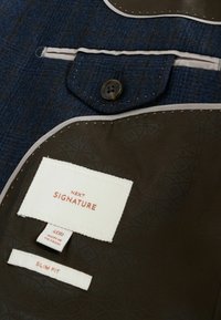 Modrá texturovaná látka s hnědým lemováním, obsahující kapsu na knoflík a štítky. Materiály zahrnují polyester a bavlnu. Design s úzkým střihem.